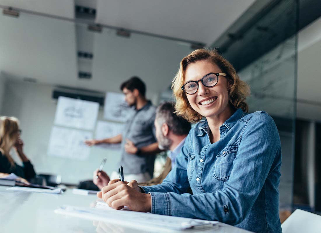 Commercial Bonds - Focus On a Young Woman Sitting in a Board Room during a Business Meeting and Smiling at the Camera with the Background Blurred