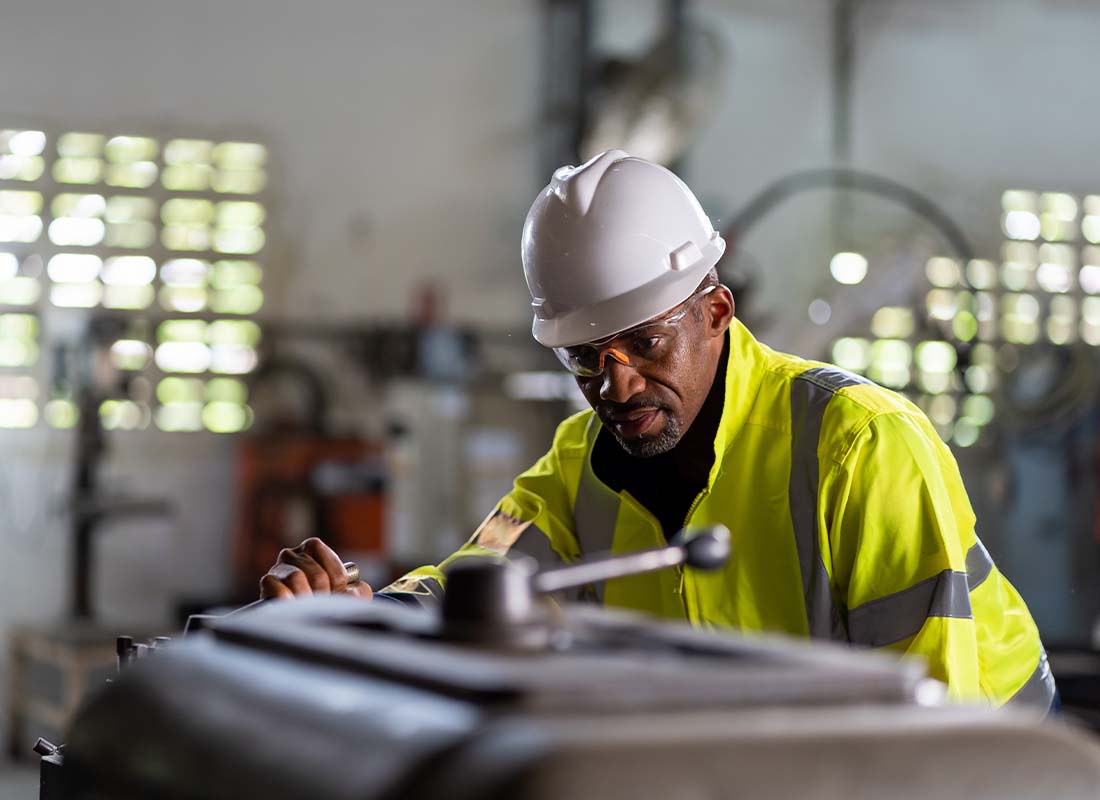 Mechanical Contractor Insurance - Male Engineer Performing Maintenance on Heavy Machine in the Factory in a Safety Uniform With Goggles and Helmet