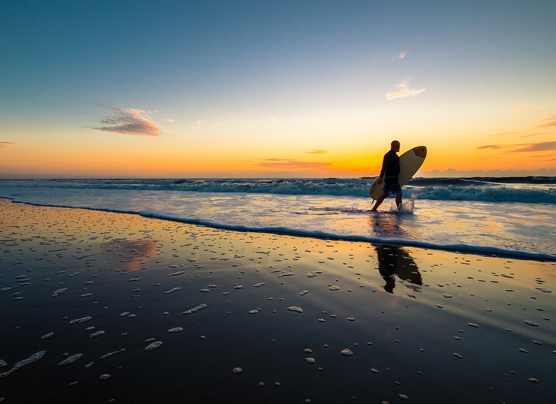 About Our Agency - Surfer Walking Down the Shore at Sunrise